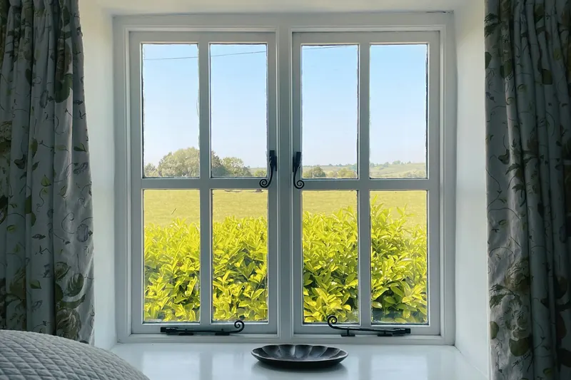 Vue depuis une fenêtre de chambre, rideaux clairs, un champ derrière la vitre.