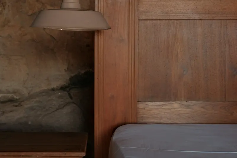 Chambre entièrement lambrissée de bois sombre, suspension métallique au-dessus de la table de chevet, niche de pierre apparente dans un coin.