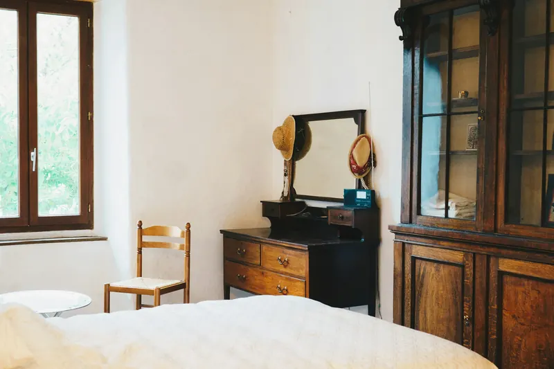 Chambre claire, lit bas en lin blanc, armoire vitrée ancienne et fenêtre à petits carreaux.