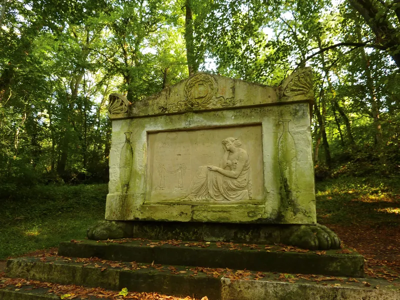 Monument de pierre sculpté et couvert de mousse, dans un sous-bois, feuilles mortes sur les marches.