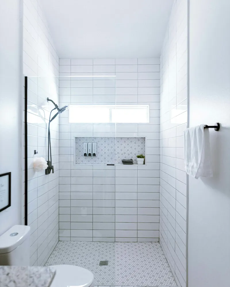 Douche à l’italienne carrelée de blanc, paroi vitrée, niche de rangement, serviette blanche suspendue.